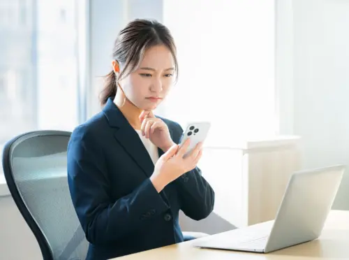 パソコン作業中にスマートフォンを見て、目の疲れを気にする女性