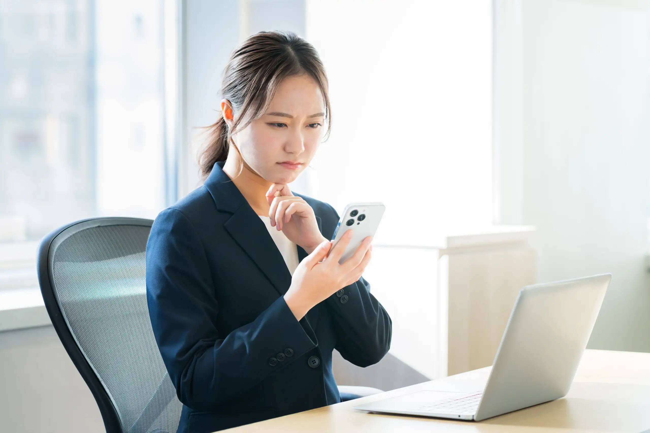パソコン作業中にスマートフォンを見て、目の疲れを気にする女性