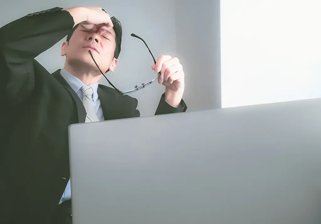 眼精疲労で目頭を押さえる男性